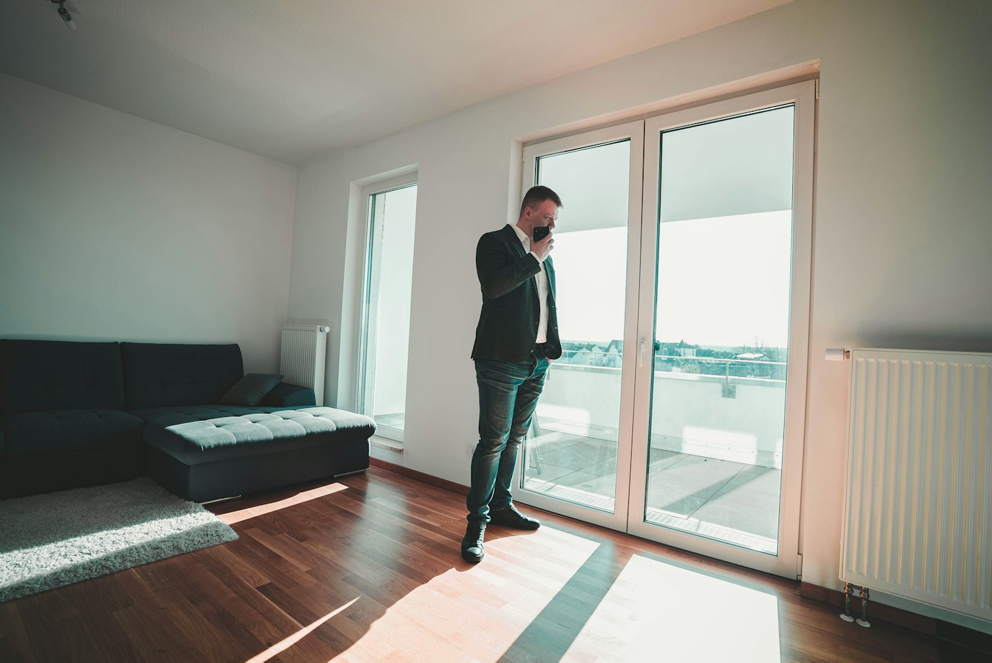 Man in suit jacket and jeans talks on smartphone in modern apartment.